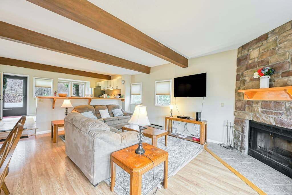 A living room with a fireplace, a sofa, a TV, and a kitchen in the background.
