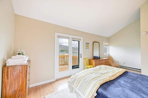 A bedroom with a bed, a wooden dresser, a mirror, and a sliding glass door leading to a balcony.