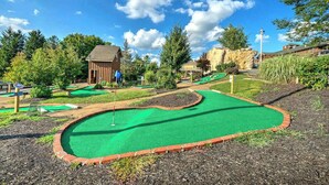 Ein Minigolfplatz mit einem grünen Putting-Bereich, einem hölzernen Gebäude und umliegenden Bäumen.