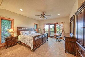 Ein Schlafzimmer mit einem Bett, Nachttischen, einem Schreibtisch, einem Stuhl, einem Deckenventilator und einem großen Fenster.