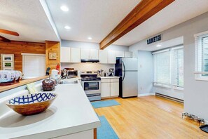 Una cocina moderna con armarios blancos, techo de madera y un amplio ventanal con persianas.