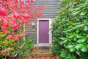 Une maison en bois avec une porte violette, une plaque portant le numéro « 21 » et un petit porche avec un paillasson.