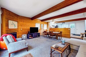 Un intérieur de chalet chaleureux, avec un revêtement mural en bois, un téléviseur, un coin repas et une cuisine.