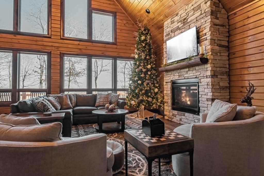 A cozy living room with a fireplace, a Christmas tree, and large windows.