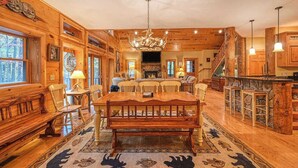 Ein Holzinterieur mit Esstisch, Stühlen, einer Chandelieber und einem Kamin.