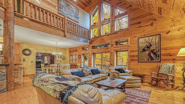 Eine geräumige Holzjagdhuette mit Schlafzimmer auf dem Dachboden, einem Essbereich und einem Wohnzimmer, möbliert mit Ledersofas und einem Kamin.