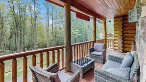 Eine Blockhütte mit einer Holzterrasse, Korbmöbeln und Blick auf den Wald.