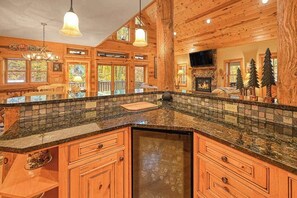 A log cabin interior with a kitchen island, wooden cabinets, and a fireplace. - Rustic 5BR Cabin - HOT TUB - Swanton (Swanton)