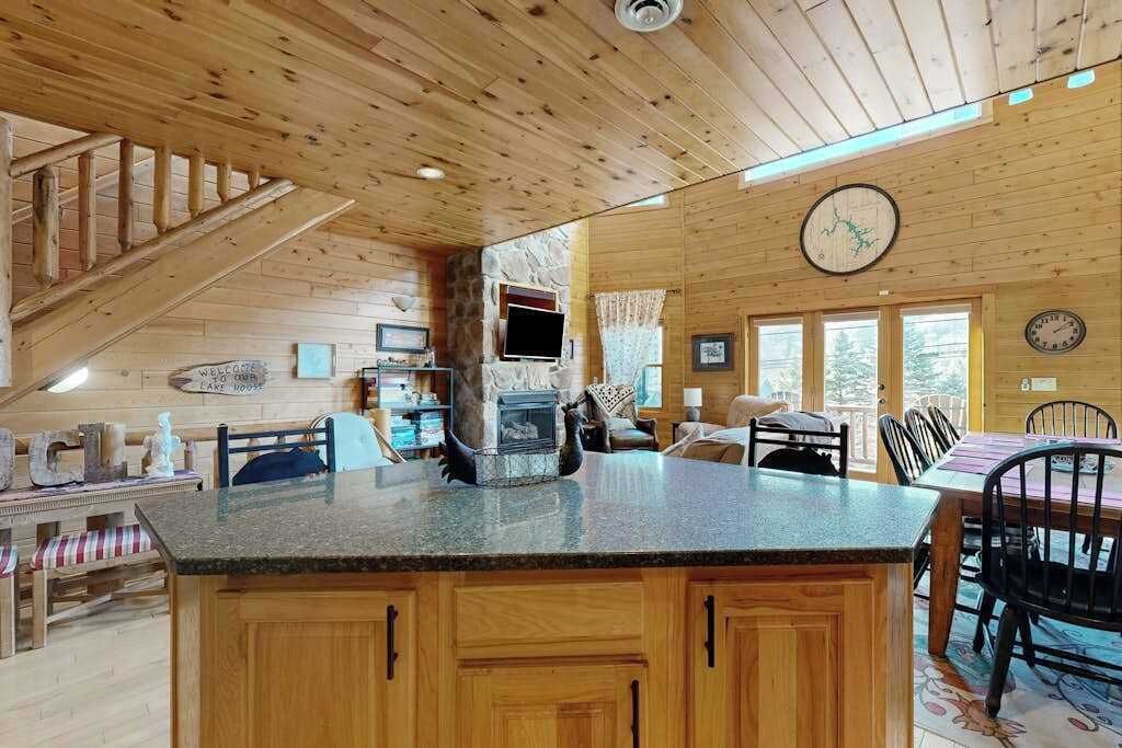 A wooden cabin interior with a kitchen island, dining area, and a fireplace.