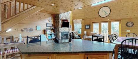 A wooden cabin interior with a kitchen island, dining area, and a fireplace.