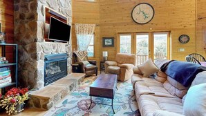 Uma sala de estar aconchegante com lareira de pedra, sofás de couro, televisão de tela plana e um relógio grande na parede.