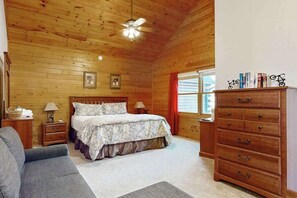 A wooden-paneled bedroom with a bed, dresser, nightstands, and a ceiling fan.