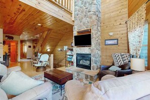 A cozy cabin interior with a stone fireplace, wooden walls, and a comfortable seating area.