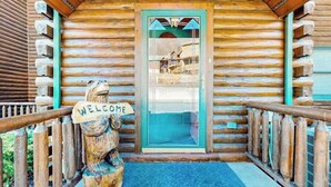 Uma cabana de madeira com uma placa de boas-vindas, uma porta de vidro e um corrimão de madeira.