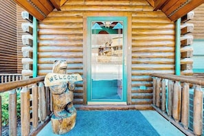 A wooden cabin with a welcome sign, a glass door, and a wooden railing.