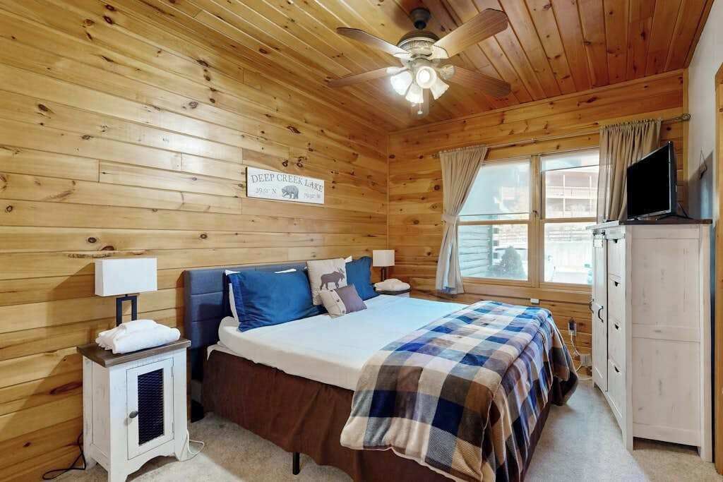 A wooden cabin room with a bed, a ceiling fan, a TV, and a sign indicating a lake view.