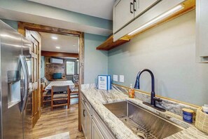 A compact kitchen with a built-in sink, a dining area with a table and chairs, and a refrigerator. - 2BR - Cozy - Lakefront - Hot Tub (McHenry)