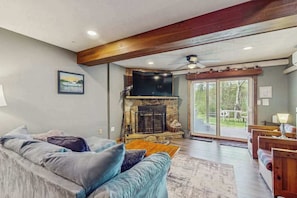 A living room with a stone fireplace, a ceiling fan, and a large window. - 2BR - Cozy - Lakefront - Hot Tub (McHenry)