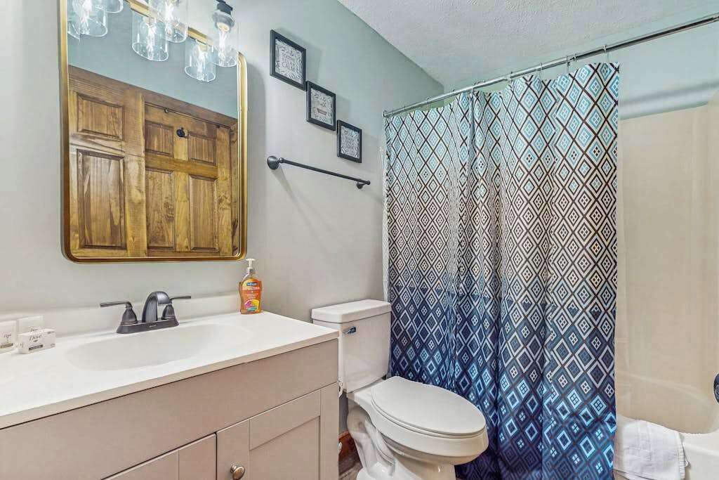 Une salle de bain avec un meuble-lavabo en bois, des toilettes blanches et un rideau de douche à motifs.