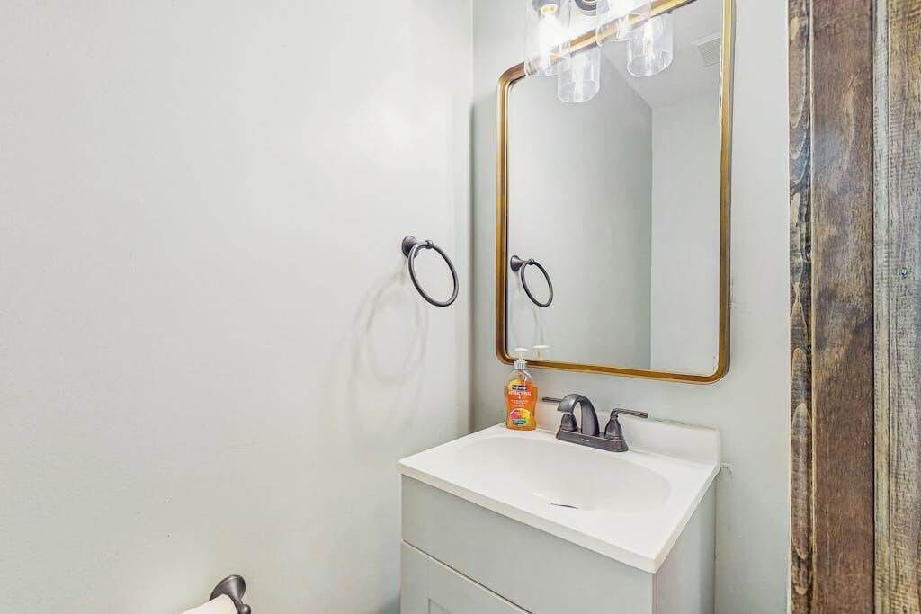 A bathroom with a white sink, a gold-framed mirror, and a soap dispenser.