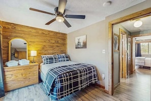Un dormitorio con cama, cabecera de madera, ventilador de techo, lámpara de noche y un espejo.