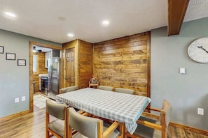 Un comedor con una pared de madera, un reloj y una mesa con sillas.