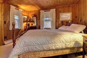 Une chambre à coucher dans une cabane en bois, avec un lit, une table de chevet, une lampe, un miroir et un tableau encadré au mur.