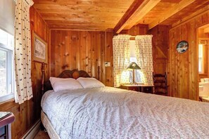 Ein Schlafzimmer einer Holzhütte mit Bett, Vorhängen, einer Lampe und einem gerahmten Bild an der Wand.