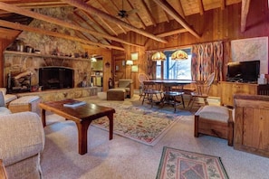 A rustic cabin interior with a stone fireplace, wooden furniture, and a dining area.