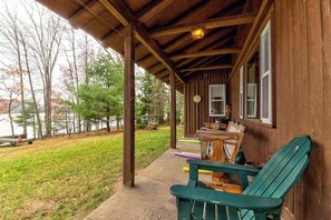 Une cabane en bois avec une véranda, un espace salon extérieur et une vue sur un lac.