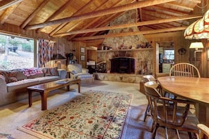 Ein gemütliches Blockhaus-Interieur mit Kamin aus Stein, Holzmöbeln und einem großen Teppich.