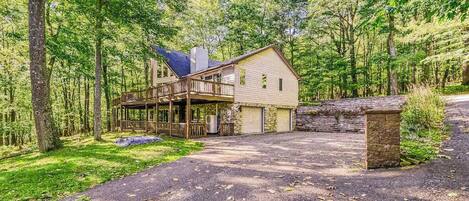 A cabin with a deck, a garage, and a stone wall.
