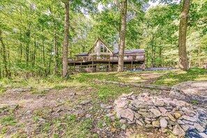 A cabin with a wooden deck and multiple levels, surrounded by a forest.