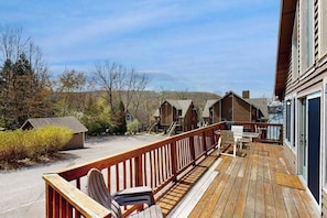 Eine Holzterrasse mit Sitzgelegenheiten im Freien, Blick auf Holzhütten und einem klaren Himmel.