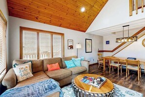 Ein gemütliches Wohnzimmer mit Holzbalkendecke, einer Sofagarnitur, einem Couchtisch und einem Essbereich mit Holzstühlen und einem Tisch.