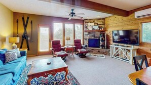 Un salon comprenant un canapé, des fauteuils, une table basse, une cheminée, un téléviseur et un ventilateur de plafond.