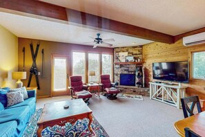Ein Wohnzimmer mit einer Couch, Sesseln, einem Couchtisch, einem Kamin, einem Fernseher und einem Deckenventilator.