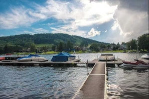 Eine Anlegestelle mit Booten, ein hölzerner Steg und ein See mit einem bewaldeten Hügel im Hintergrund.
