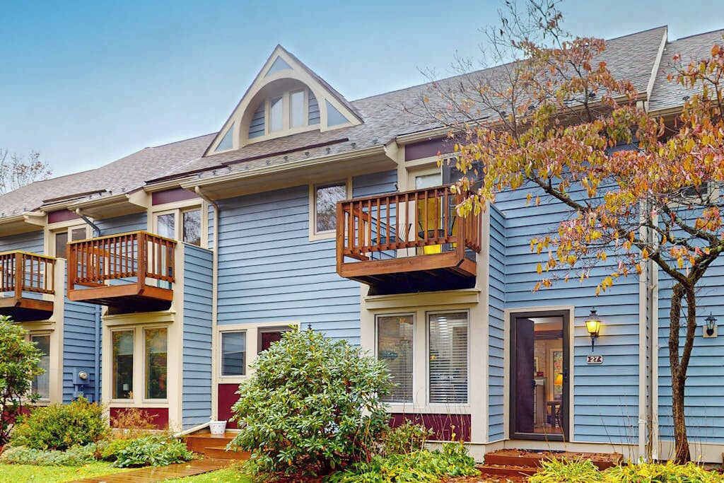 A row of blue townhouses with wooden balconies, a small garden, and a clear sky.