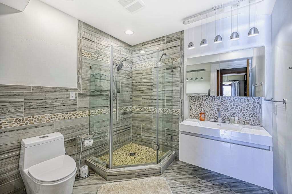 A modern bathroom with a glass-enclosed shower, a white toilet, and a white vanity with a mirror.