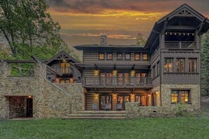 A large, multi-story log cabin with a stone foundation, multiple balconies, and a prominent chimney. - Lakefront 7BR Chalet - HOT TUB - Swanton (Swanton)