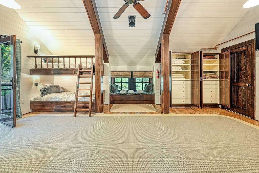 Ein Schlafzimmer im Spitzgeschoss mit Schlafbox, einer Leiter, einer eingebauten Sitzbank und einem Kleiderschrank mit Regalen.