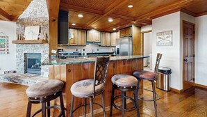 Una cocina con chimenea de piedra, techo de madera y una zona de bar con taburetes.