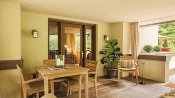 A wooden deck with a table and chairs, a potted plant, and a view of greenery outside.