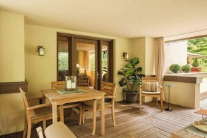 A wooden deck with a table and chairs, a potted plant, and a view of greenery outside.