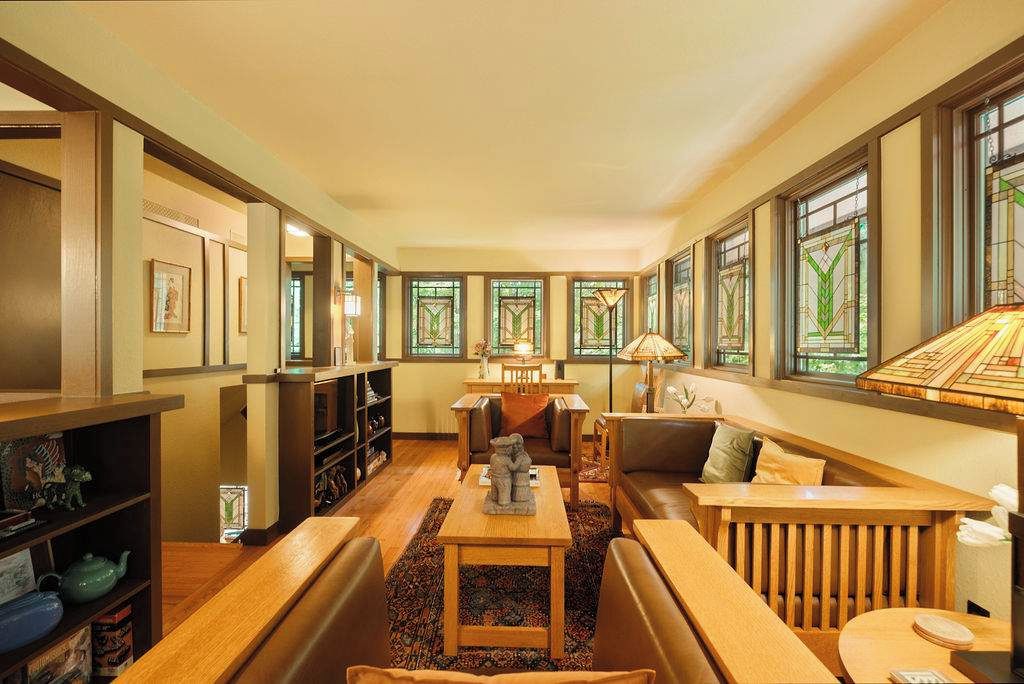 A cozy living room with a fireplace, comfortable seating, and large windows with stained glass.