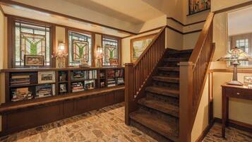 A library with bookshelves, a staircase, and a stone floor.