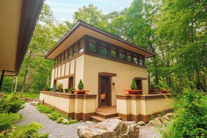 A two-story building with a symmetrical facade, a central entrance, and a surrounding garden with potted plants.
