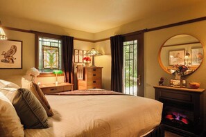 A hotel room with a large bed, a fireplace, a mirror, and a window with curtains.