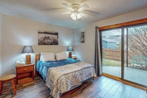 A bedroom with a bed, two bedside tables, a ceiling fan, and a large sliding glass door leading to an outdoor area.